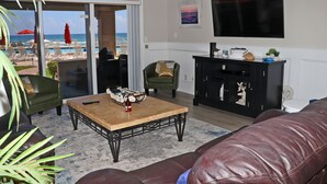 A living room with a view of the beach, a fireplace, and a flat-screen TV. - Steps to south pool deck, pool and ocean from this ground floor, three bedroom, three bath sleeps 8. (New Smyrna Beach)