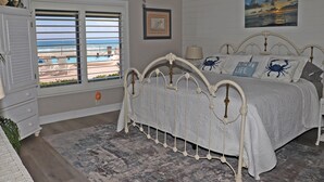 A bedroom with a bed, a window with a view of the beach, a ceiling fan, and a framed picture on the wall. - Steps to south pool deck, pool and ocean from this ground floor, three bedroom, three bath sleeps 8. (New Smyrna Beach)