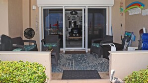 An outdoor seating area with wicker furniture, a fan, and a view into a kitchen. - Steps to south pool deck, pool and ocean from this ground floor, three bedroom, three bath sleeps 8. (New Smyrna Beach)