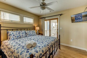 A bedroom with a bed, ceiling fan, window blinds, and a view of the outside.