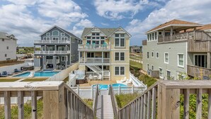 A coastal residential area with multiple two-story houses, a wooden deck, and a swimming pool. - Tipsy Mermaid | Oceanfront | Private Pool, Hot Tub | Nags Head (Nags Head)