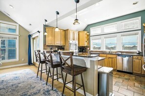 A kitchen with wooden cabinets, a central island, and a view of the outdoors through large windows.