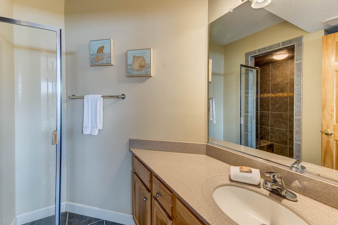 A modern bathroom with a glass shower enclosure, a beige vanity with a sink, and two framed artworks on the wall.