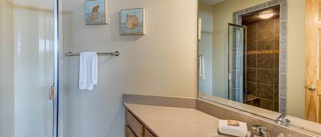 A modern bathroom with a glass shower enclosure, a beige vanity with a sink, and two framed artworks on the wall.