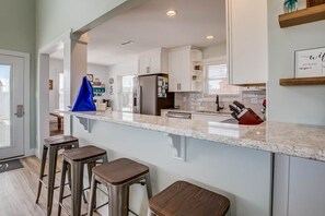 A modern kitchen with white cabinets, a marble countertop, and stainless steel appliances. There are three stools at the counter.