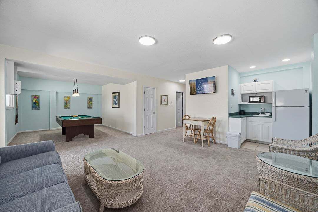 A living room with a pool table, a dining area, and a kitchenette.