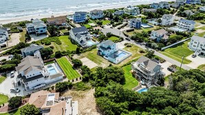 Vue aérienne d’un quartier résidentiel situé sur la côte, avec des maisons, des pelouses et une plage.