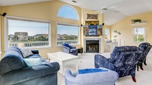Un salon spacieux doté d’une cheminée, de grandes fenêtres et d’un balcon offrant une vue sur les maisons.