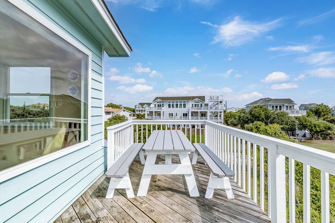 A wooden deck with a picnic table, white railings, and a view of houses in the background.