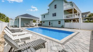 Une maison à deux étages avec une piscine, un espace salon extérieur et un patio couvert.