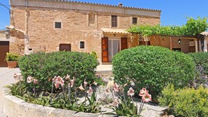 A stone building with a tiled roof, a wooden door, and a small window. There are potted plants and flowers in front of the building. - Historic finca with modern comfort and panoramic views, pool, calm nature, WiFi (Son Serra de Marina)
