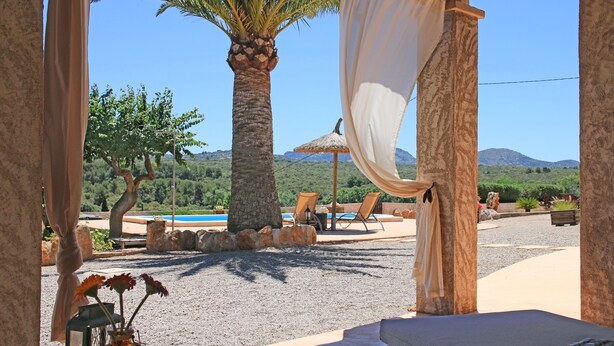 A covered outdoor seating area with a pool, palm trees, and a mountain view. - Historic finca with modern comfort and panoramic views, pool, calm nature, WiFi (Son Serra de Marina)