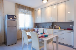 Una cucina moderna con mobili bianchi, forno a microonde integrato e zona pranzo con quattro sedie bianche e tavolo apparecchiato per quattro persone.