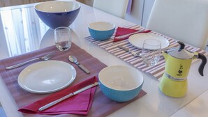 Une table à manger dressée avec des assiettes, des bols, des couverts et une cafetière.