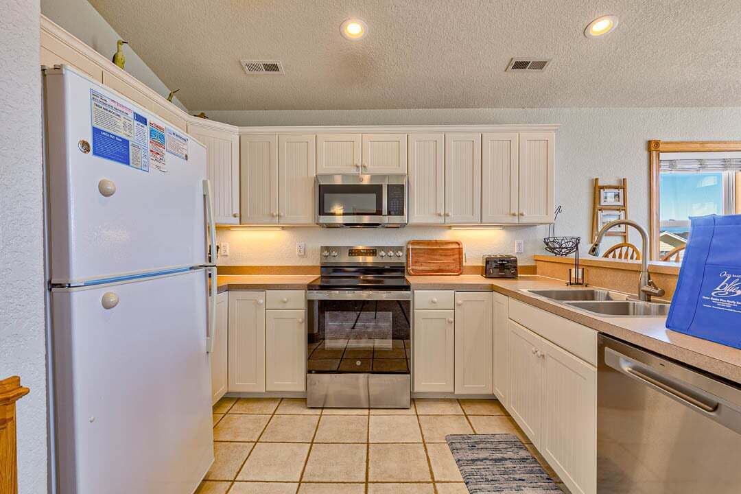 A compact kitchen with white cabinets, a stainless steel refrigerator, microwave, oven, and dishwasher.