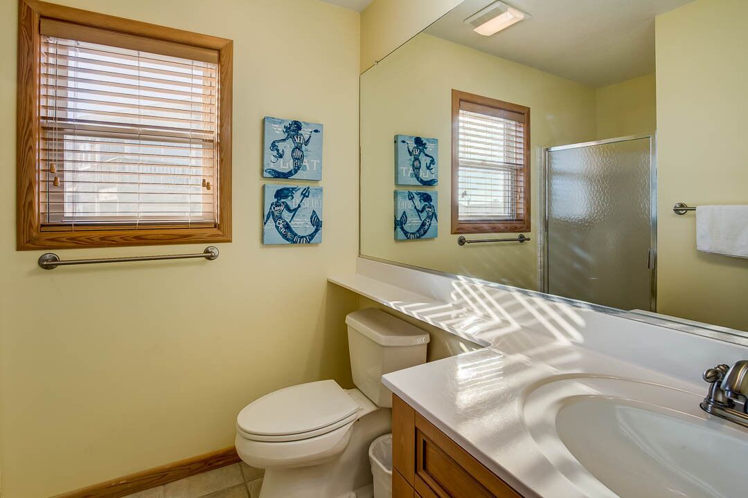 A bathroom with a toilet, sink, and shower. There are three blue artwork pieces on the wall.