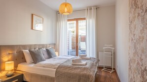 Un dormitorio con cama, mesita de noche, lámpara y vistas al exterior.