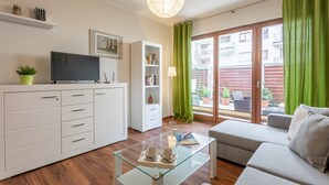 Una sala de estar moderna con un sofá, una mesa de centro de vidrio, un televisor, una estantería y un ventanal corredero que da a un área exterior.