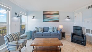 A living room with a sofa, striped armchair, and a black leather chair. There is a wooden coffee table in the center. - Beachfront Escape | Ocean Views, Heated Pool & Hot Tub (Corpus Christi)