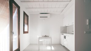 Une cuisine lumineuse et épurée, avec des meubles blancs, un îlot central et une porte-fenêtre coulissante donnant sur un espace extérieur.