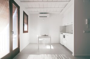 A bright, white interior with a table and chairs, a kitchen area, and a sliding glass door. - Estudio Casco Antiguo II Inmomart (Peñiscola)