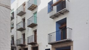 Une rue étroite bordée d’immeubles blancs, de balcons et de portes bleues.