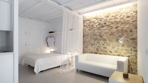 Une chambre à coucher avec un lit, un canapé blanc, un mur en pierre et une petite table avec une lampe.