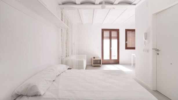 Une chambre à coucher au style minimaliste, avec un grand lit, une table de chevet, une armoire et une porte donnant sur une autre pièce.