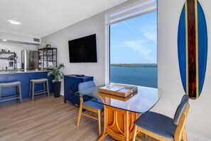 A modern kitchen with a built-in refrigerator, a dining area with a glass table and chairs, and a large window offering a view of the water.
