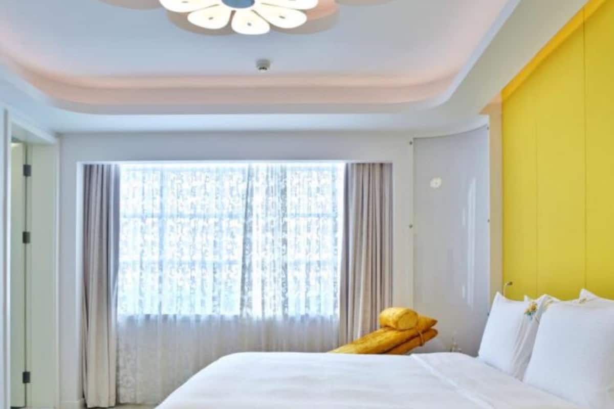 A hotel room with a large bed, a window with curtains, and a yellow accent wall.