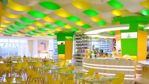 A brightly lit restaurant with yellow chairs and tables, a counter with a staff member, and a ceiling with green and white panels. - Floloving Hotel (Guangzhou)
