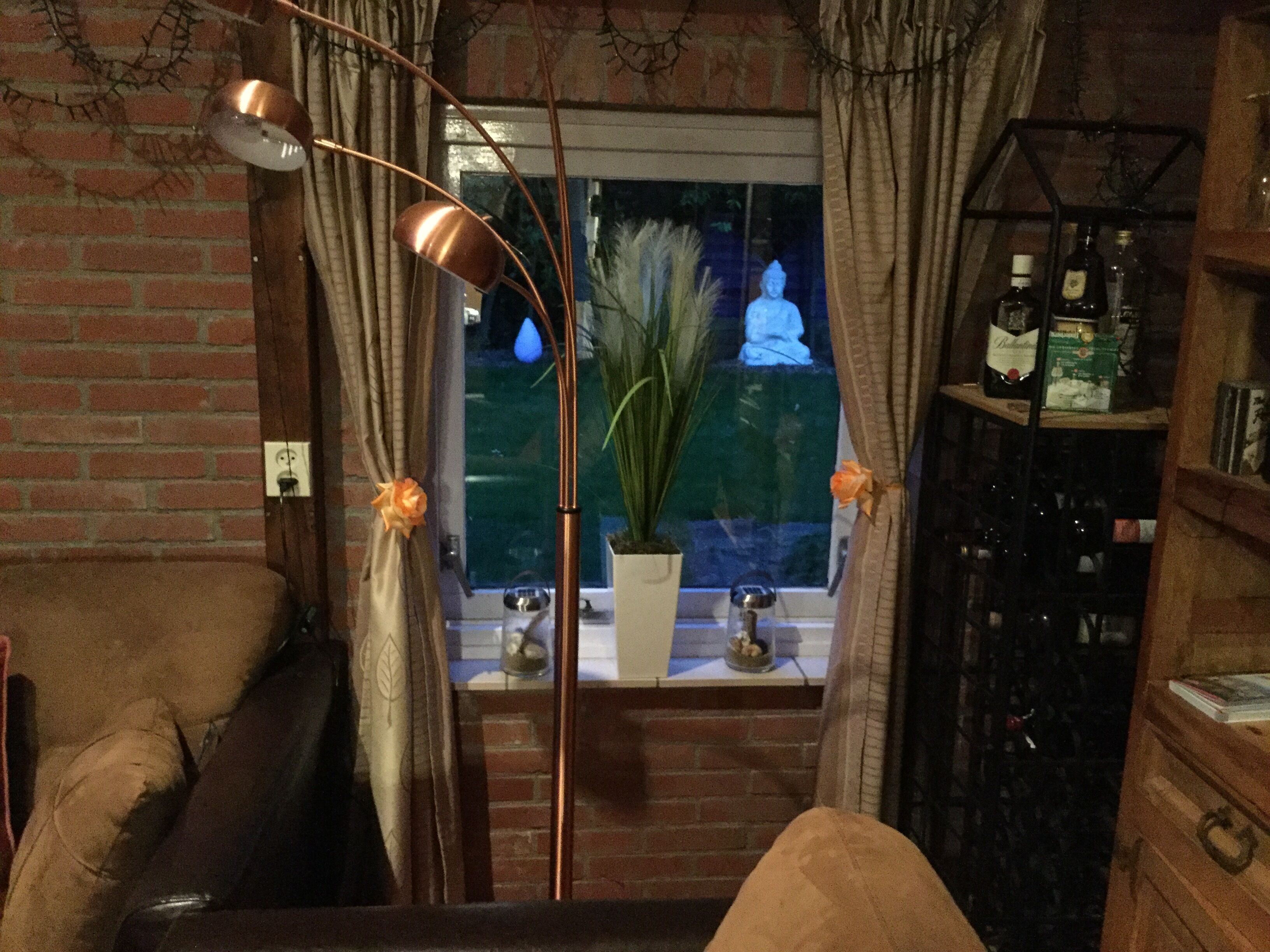 Een gezellige woonkamer met een bakstenen muur, een leren bank, een bijzettafeltje, een potplant en een raam met uitzicht op een standbeeld.
