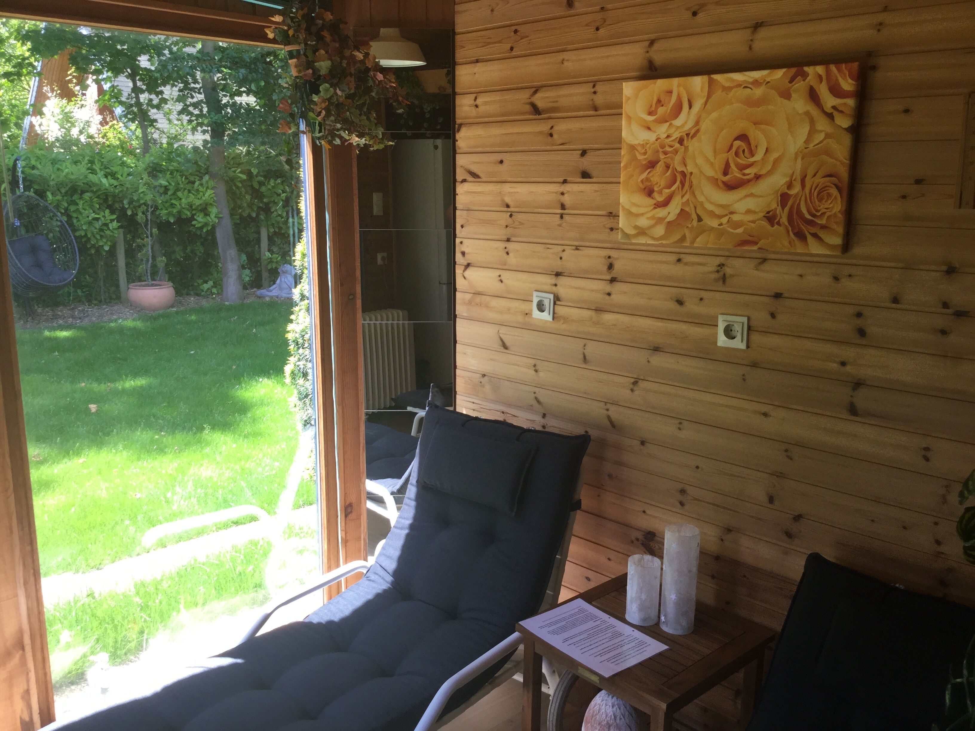 Une pièce en bois avec un seul fauteuil, une petite table avec des bougies et un grand tableau représentant des fleurs accroché au mur.
