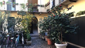 Pátio com bicicletas, plantas em vasos e entrada de um edifício.