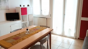 Un área de comedor con una mesa, sillas, un televisor en un mueble y una ventana con cortinas.