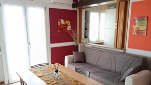 Un comedor con una mesa de madera, sillas, un sofá y una pared roja con un cuadro floral.