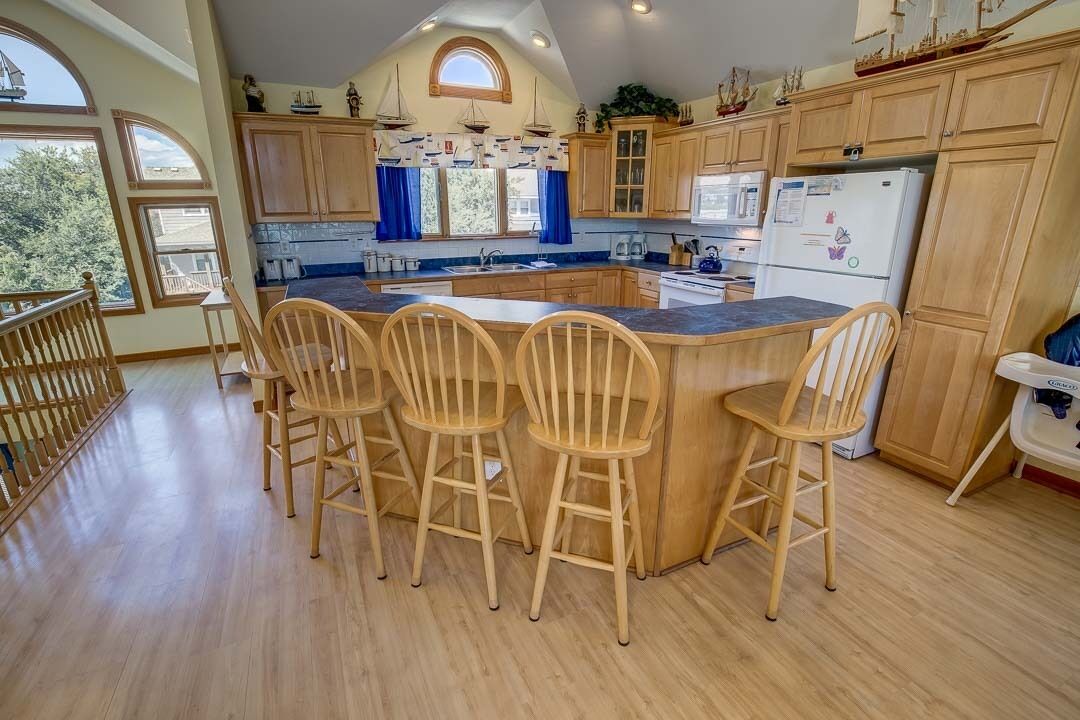 A kitchen with wooden cabinets, a central island with bar stools, and a view of the outdoors through large windows.