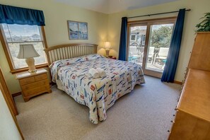 A bedroom with a bed, a nightstand, a lamp, a window with curtains, and a view of the outside.