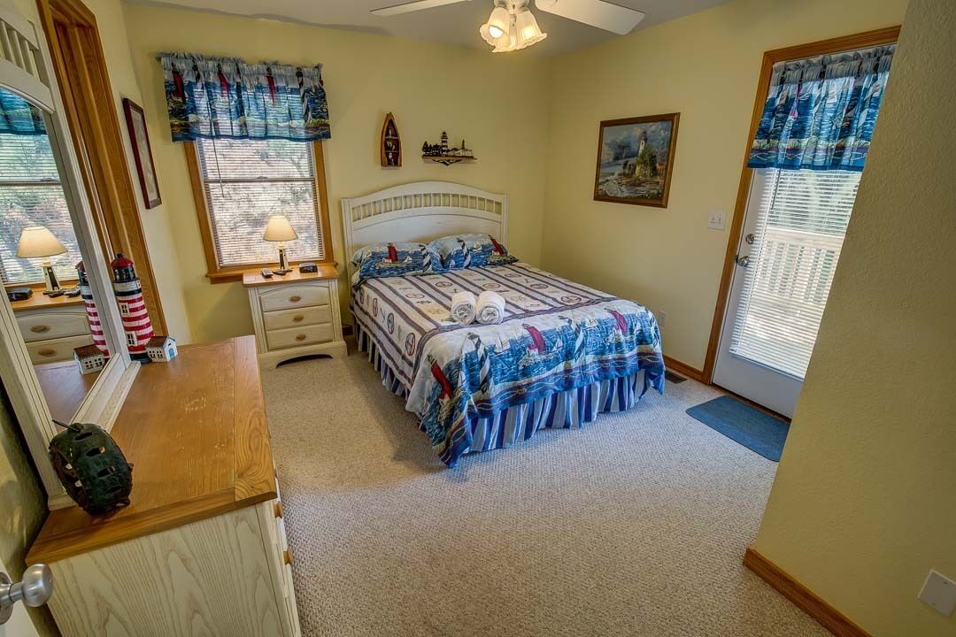 Une chambre à coucher avec un lit, des tables de chevet, une commode, un miroir et une fenêtre avec des rideaux.