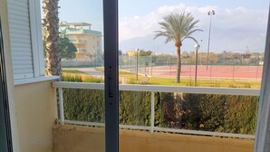 A balcony with a view of a sports field, palm trees, and buildings in the distance. - PARQUEMAR VIII BL. II 1º SOLO FAMILIAS! (Xeraco Playa)