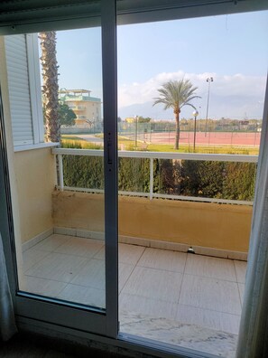 A balcony with a view of a sports field, palm trees, and buildings in the distance.