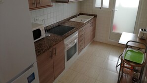 A kitchen with wooden cabinets, a microwave, a stove, and a sink. - PARQUEMAR VIII BL. II 1º SOLO FAMILIAS! (Xeraco Playa)