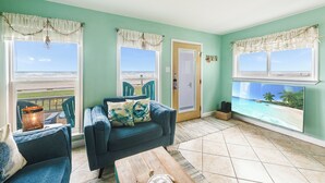 A living room with a view of the ocean, a blue sofa, and a wooden coffee table. - Beachfront Escape | Pool, Hot Tub & Ocean Views (Corpus Christi)