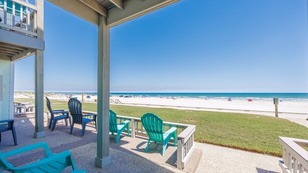 A covered outdoor seating area with chairs and tables, overlooking a beach. - Beachfront Escape | Pool, Hot Tub & Ocean Views (Corpus Christi)