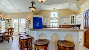 Una cocina amplia con una isla grande, taburetes de madera y armarios blancos.