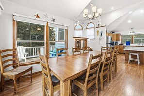 A spacious dining area with a wooden table and chairs, a kitchen with wooden cabinets, and large windows with a view of the outdoors.