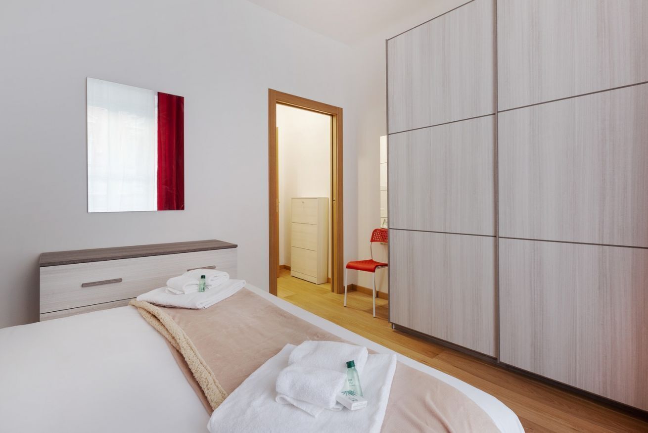A hotel room with a bed, a wardrobe, a mirror, and a door leading to a bathroom.