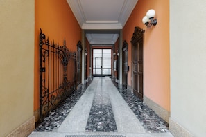 Un pasillo con piso de mármol, puertas metálicas ornamentadas y una puerta al final.