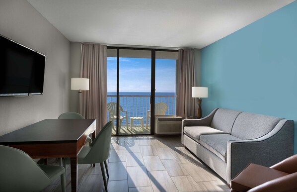 A hotel room with a balcony, a TV, a sofa, a table, and two chairs.