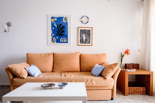 Un salon avec un canapé beige, une table basse blanche et une petite table d’appoint en bois sur laquelle est posé un vase de fleurs.